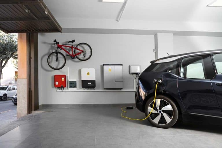 Electric black vehicle using electric car charging station at home. Particular Electric Vehicle Charging Station at home garage with bicycle hanging on the wall. Copy-space, Horizontal.