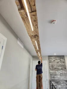 Ottawa Electric technician installing integrated LED lighting in a custom wood ceiling beam at a Greely home.