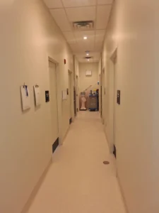 Dental & Plastic Surgery Facility clinical corridor with recessed ceiling lights, room signage, ceiling devices, and finished medical electrical fit up.