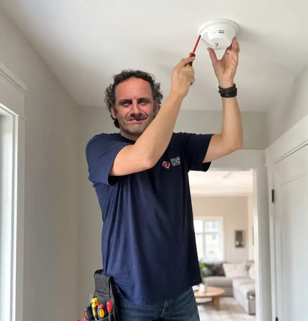 Licensed Ottawa Electric electrician testing a ceiling mounted smoke and carbon monoxide alarm inside a bright modern home hallway.